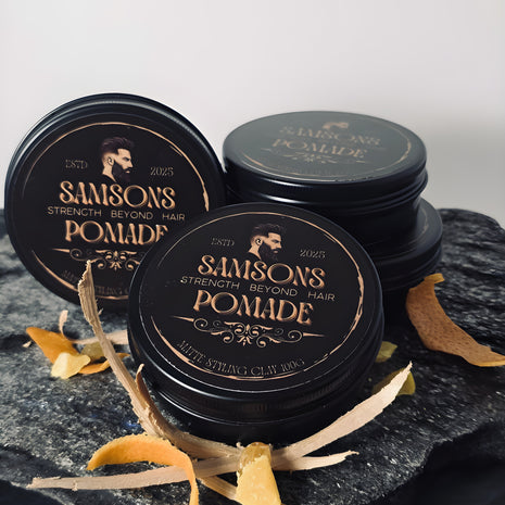 Three jars of Samson's Pomade on a dark surface with decorative elements. orange, cedar wood, frankincense